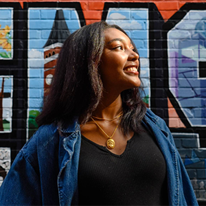 A person smiling in front of a mural