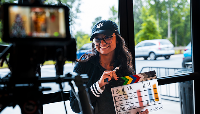 A person smiling and holding a film clapper