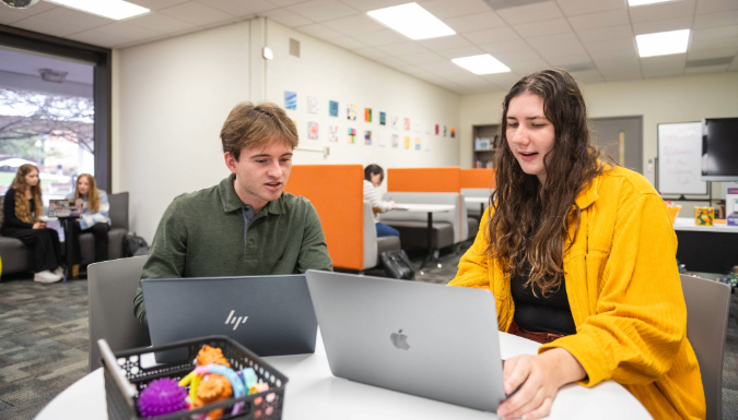 Two people talking at a table with laptops