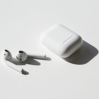 Airpods laying next to their case on a white table.
