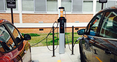 Two electric vehicles parked with a chargepoint between them charging both vehicles. 
