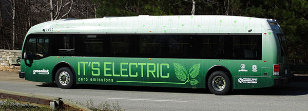 Green bus with a white top and the words it's electric in large light green font going across the side 