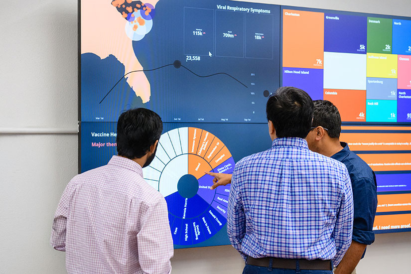 Three individuals looking at large monitor with health data displayed.