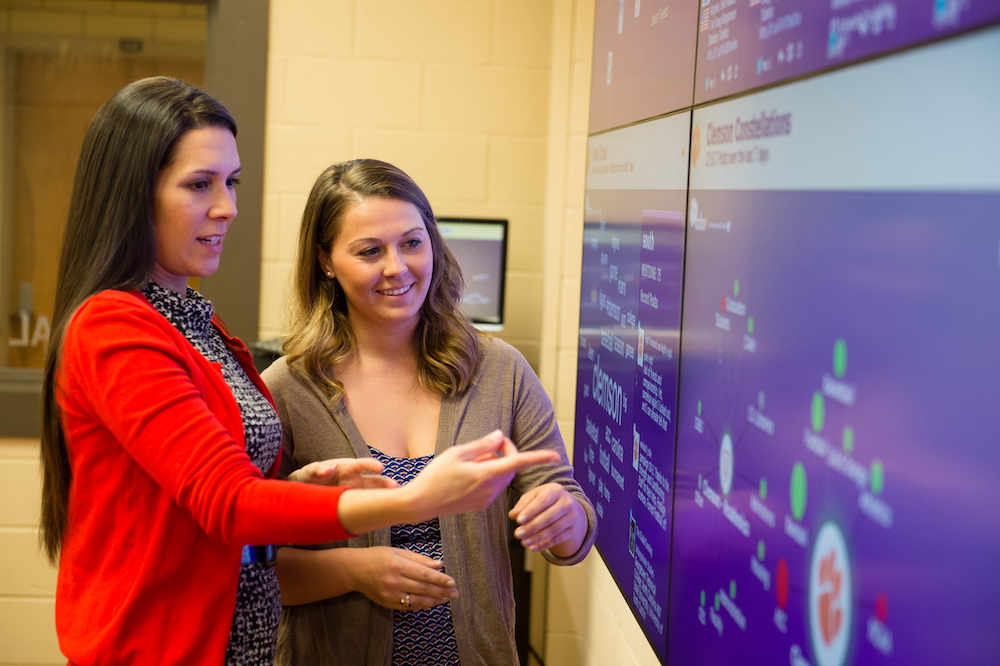 Two Women standing in front of monitors showing unknown data.