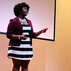 Woman standing on stage speaking.