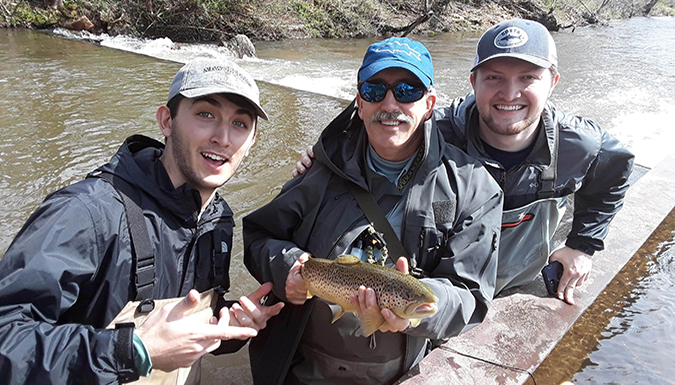 Picture of fly fishing instructor Mike Watts with two students and a fish they caught.