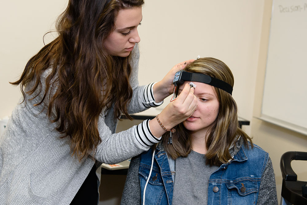 Image of a student attending to another student who is wearing an electronic device on her head