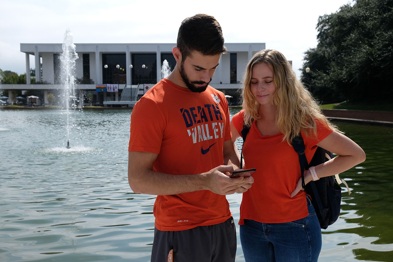 Two students looking at a cell phone in front of the reflection pond.