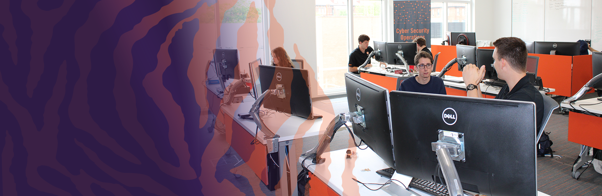 Student interns working in the Cybersecurity Security Operations Center working at desks with multiple computers and monitors.