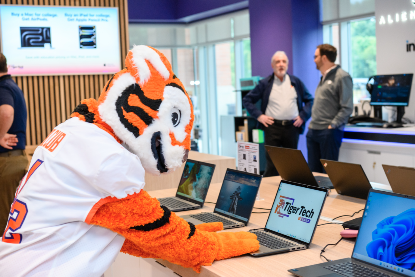 The cub mascot looking at a laptop in the Tiger Tech Shop on campus.