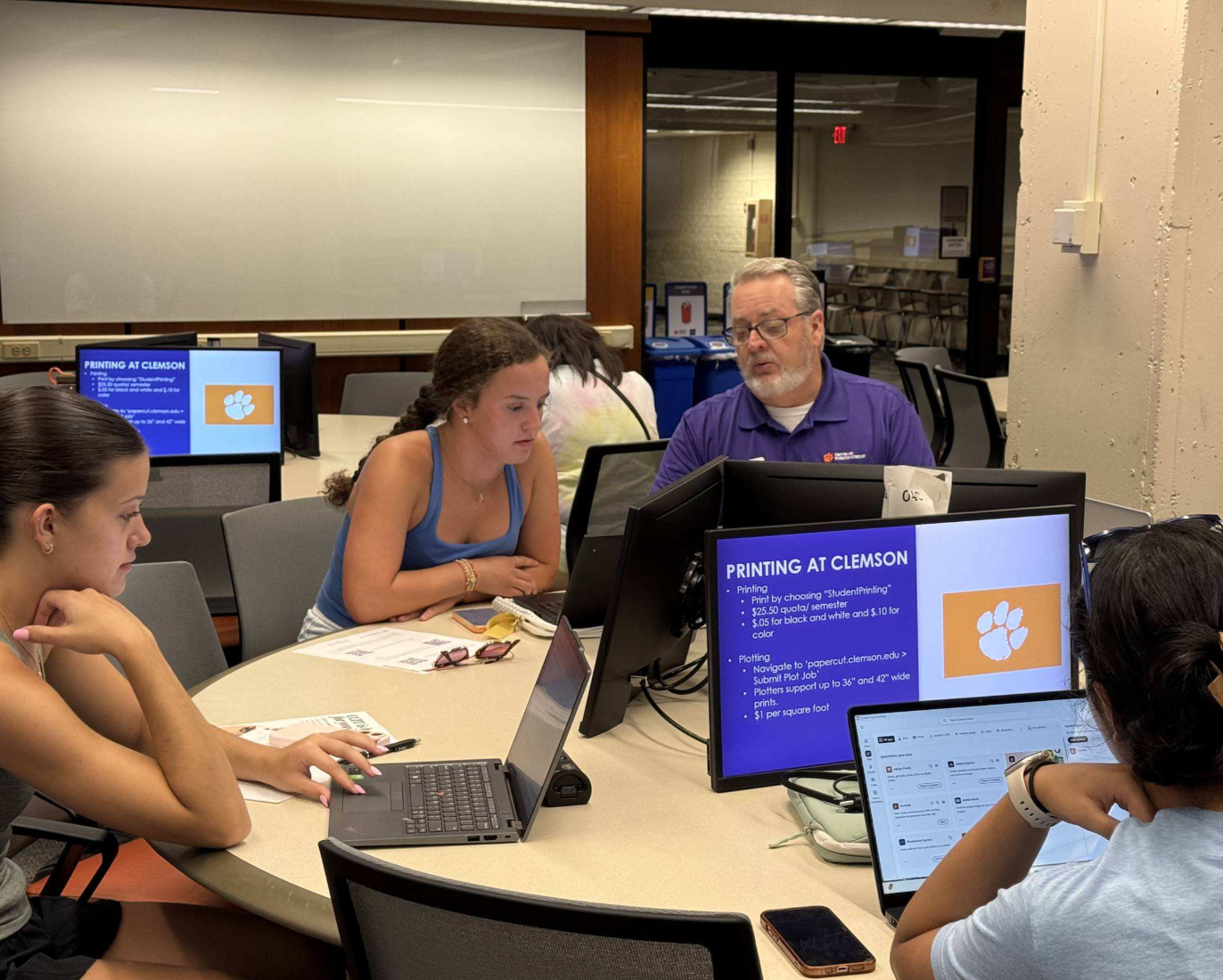 Students sitting at a table with their laptops being instructed on how to use them.