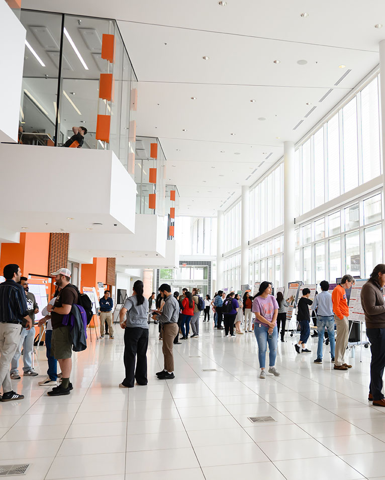 A crowd of people in the Watt Center with research posters presented throughout the main area.
