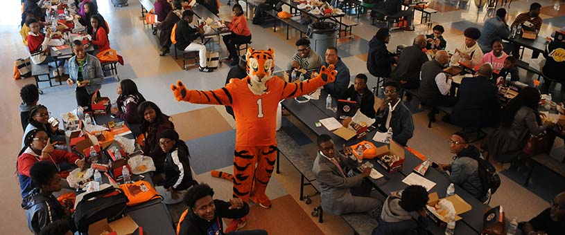 The Clemson Tiger mascot surrounded by tables full of students. 