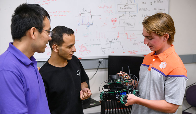 Professor Cheng with two students as they test out motorized robotic car.