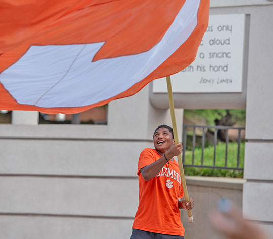 Student waving a large Clemson C flag in the arena near the Reflection Pond. 