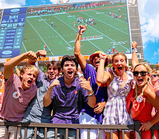 Excited group of students at a Clemson game, dressed in orange and purple.