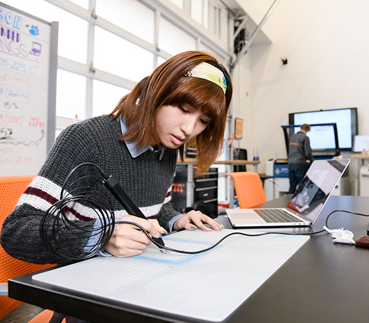 Student in Makerspace with 3D pen and laptop.
