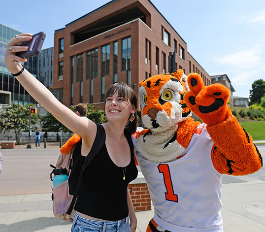 Student and Clemson Tiger taking selfie together on campus.