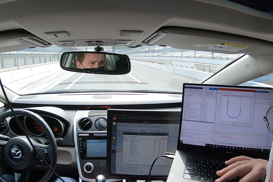 Team members sit inside a vehicle looking at a laptop.