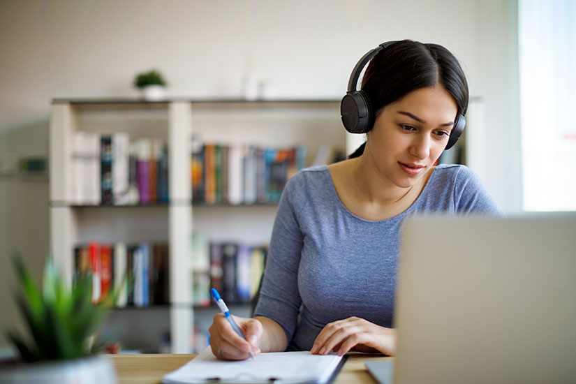 Female taking online classes on laptop with headphones.