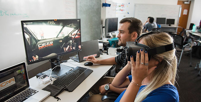 Two students looking at computer, one with VR headset on.