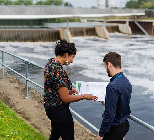 Female and male engineers discussing plans near waterway.