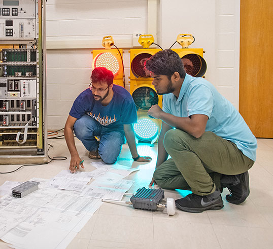 Graduate researchers viewing system plan, illuminated by a set of traffic lights.