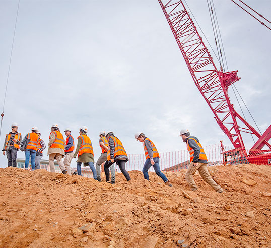 Students adn Faculty ascend dirt bank on campus construction site.