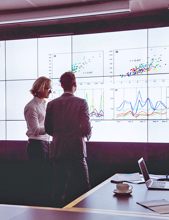 Two people looking at digital screen of figures and graphs.