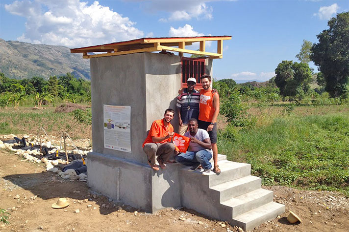 A research group in Haiti gathered near a building in a field.