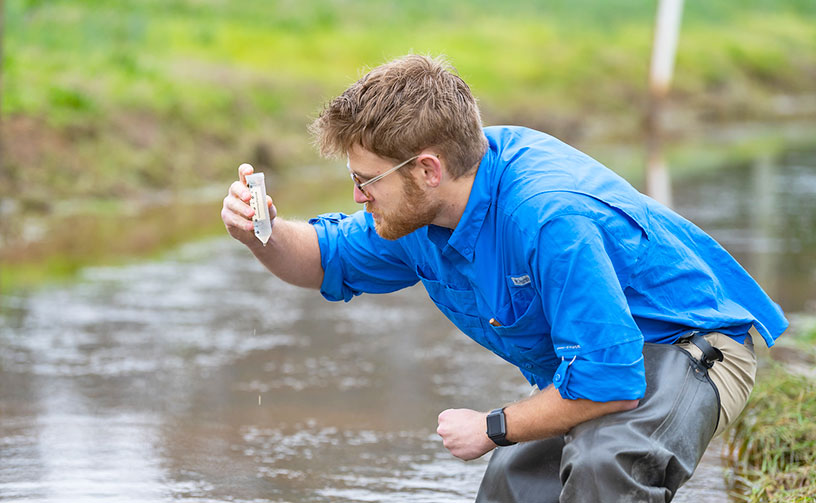 Student collecting sample from stream for testing.