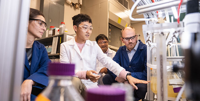 Student and professors in lab looking at equipment.