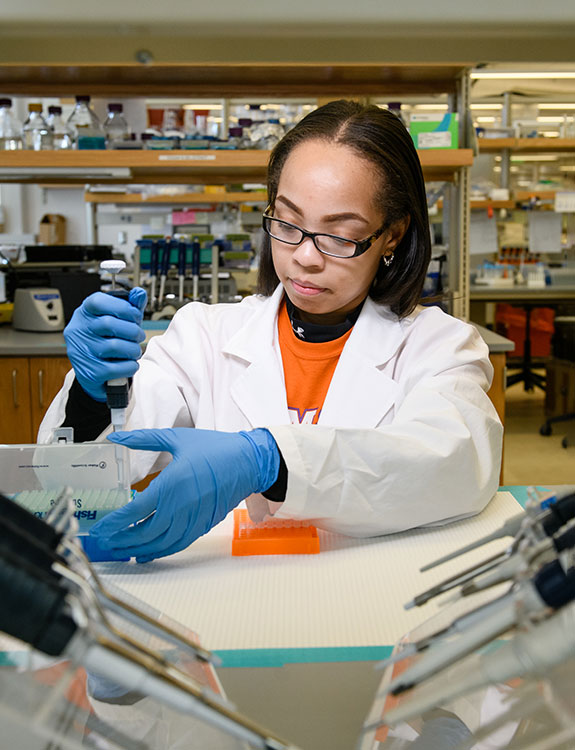 Female in lab using pipette.