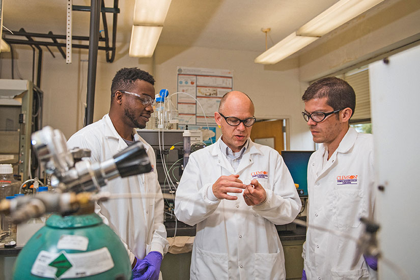 Husson and two students in lab with robotic arm.