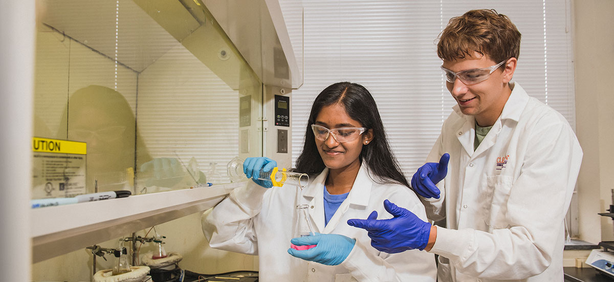 Female student filling beaker with male student pointing at fill line.