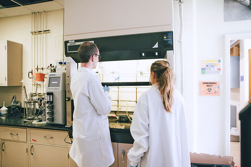 Two students in lab coats at hood.