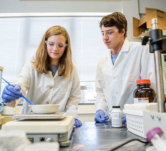 Female and male students in lab weighing powder.