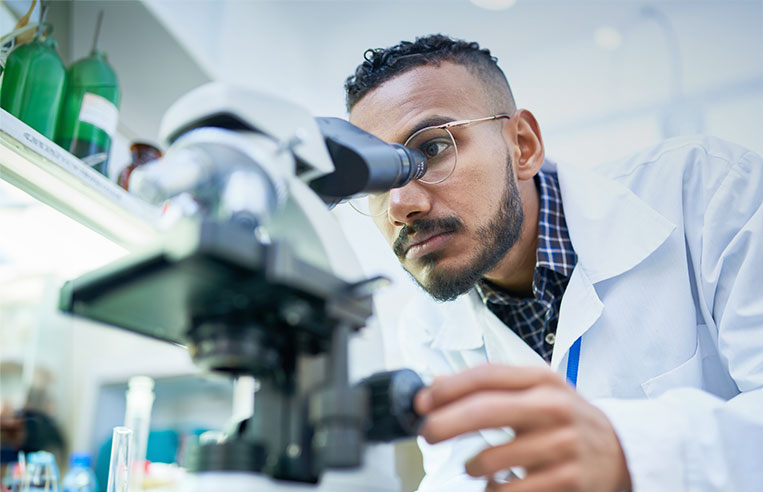 Scientist in lab peering through microscope.