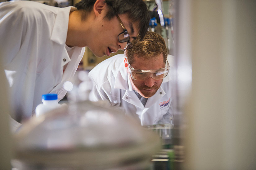 Birtwistle in lab with student peering at experiment.