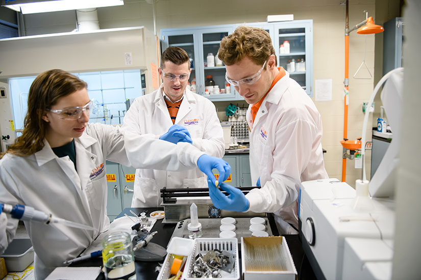 Davis in lab with student who is adding substance into equipment.