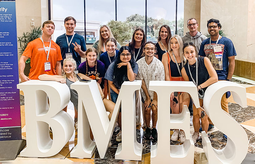 Students involved in bmes convention gather in front of sign.