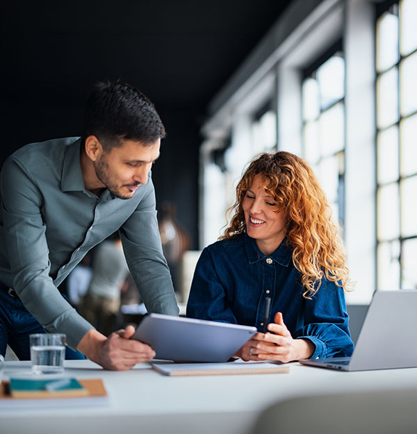 Female employee in front of laptop, listening to colleague as he provides data points.