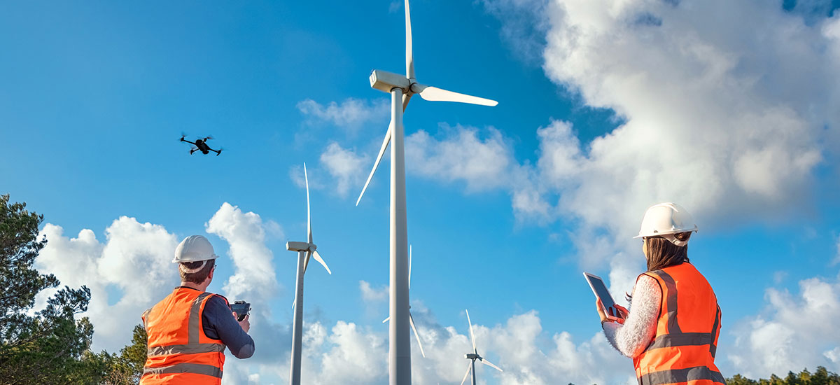 Man and woman looking out at horizon where large wind turbines are aligned.