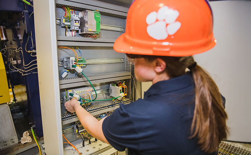 Female lab student wearing orange helmet with Clemson paw on it