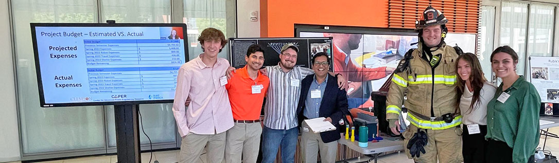 Group of students standing with fireman during senior design showcase.
