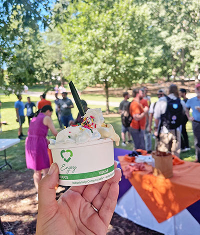 Cup of ice cream in foreground with students gathered in park behind.
