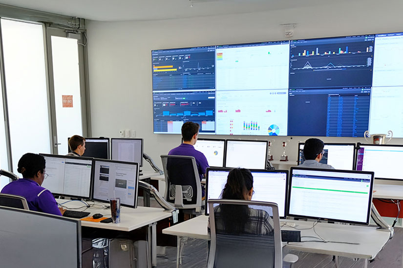 Individuals sitting at computers with large screens on wall in Cybersecurity Center