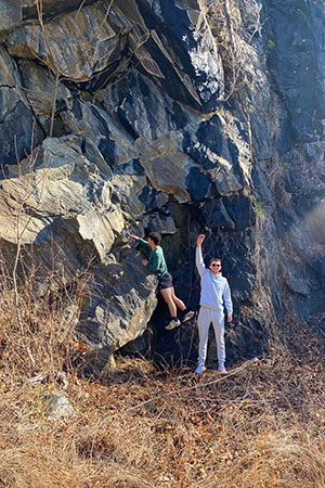 Two students near rocky wall, one measuring and one holding up specimen.