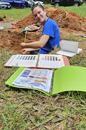 Female student smiling while partially inside hole in the soil.