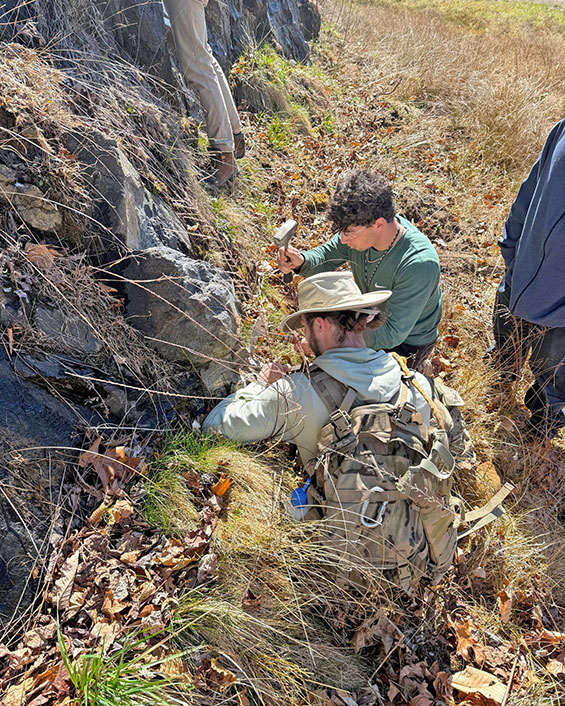 Two students taking measurements in a rocky area.
